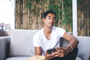 Tired Hispanic guy using smartphone in cozy cafe