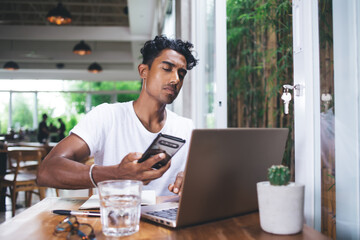 Concerned male browsing laptop and surfing mobile in eatery