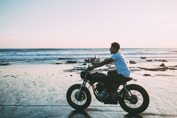 Fototapeta na wymiar Young male biker sitting on motorcycle on beach