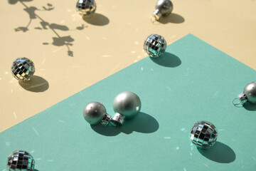 Mirror balls and silver Xmas baubles on mint green and yellow layered paper. Geometric Christmas background, isometric view with shadows