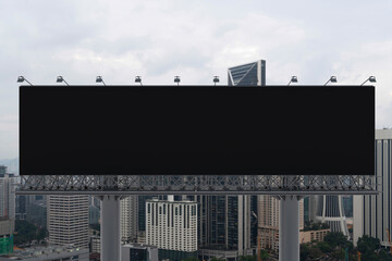 Blank black road billboard with Kuala Lumpur cityscape background at day time. Street advertising poster, mock up, 3D rendering. Front view. Concept of marketing to promote or sell services or ideas.