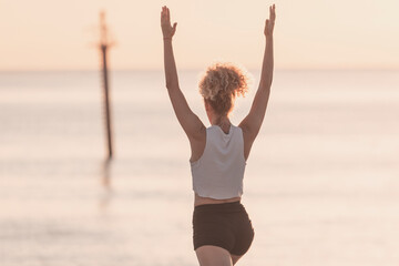 Obraz premium A young girl performs yoga exercises in front of the sea at sunrise