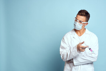 Doctor holds a syringe in his hand with a red liquid on a blue background medical gown and a protective mask