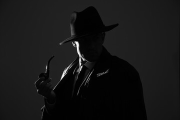 Old fashioned detective with smoking pipe on dark background, black and white effect