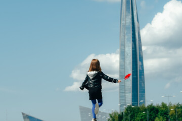 Fototapeta na wymiar Happy child with red wind spinner on sky urban background.