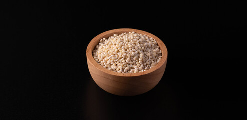Barley in a wooden cup on a black background. Copy space.