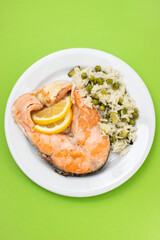 fried salmon with rice with vegetables on white plate on green background