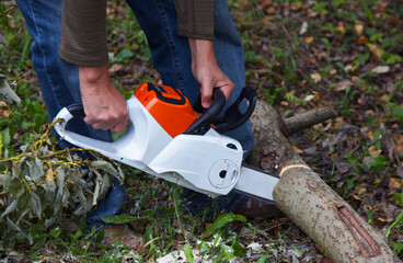 Obraz premium Close up photo of a lumberman with an electric saw cuts a log. Lumberjack at work. Technique of working with the tool.