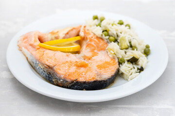 fried salmon with rice with vegetables on white plate on ceramic background