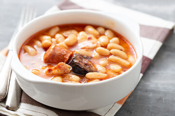 typical spanish dish fabada, beands with smoked sausages and meat on white bowl
