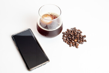 A glass of coffee grinder with coffee beans and black screen mobile phone on white background