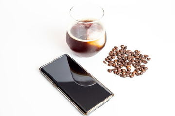 A glass of coffee grinder with coffee beans and black screen mobile phone on white background