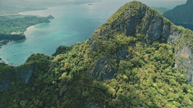 Mountain top with green tropic forest at ocean harbor. Aerial birds-eye view of vessels, boats, ships on azure water. Nobody Asia nature landscape at cloudy summer day. Cinematic drone shot