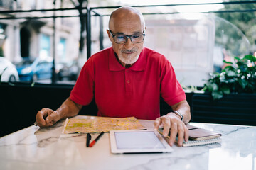 Serious man with tablet and map sitting in cafe