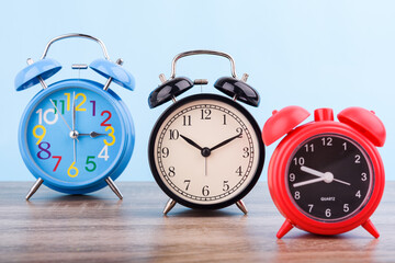Three retro Alarm clock  put on wooden table isolated on blue pastel background.