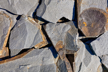 Large slabs of rocky gray sandstone with fractures and rust stains in bright sunlight.