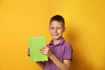 Happy little boy with book on yellow background