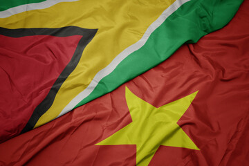 waving colorful flag of vietnam and national flag of guyana.
