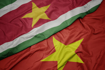 waving colorful flag of vietnam and national flag of suriname.