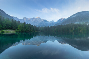 Fototapeta na wymiar Mirror reflection in Lago di Fusine, Italy. Summer spring colors and Mangart mountain in the background at sunrise in Italien Alps.Beautiful peaceful nature scenery,turquoise water,travel background.