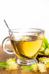 transparent glass cup of herbal tea on a white background, linden flowers are around the cup, alternative medicine