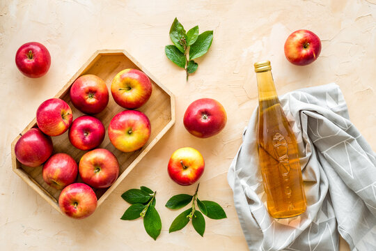 Apple cider vinegar in glass bottle and wooden tray with red apples