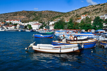 Fototapeta na wymiar white colorful ships and boats in water at piers among houses of town balaclava near rocks of mountains, reflections in ripples