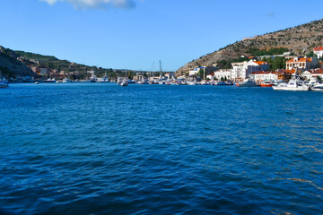 Fototapeta premium blue water with waves in bay of mountain town of Balaklava with marinas, ships, boats and bright buildings, ripples, sunny