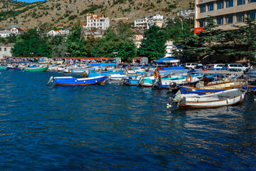 Fototapeta na wymiar colorful ships and boats in water at piers among houses and buildings of town balaclava near mountains, reflections in ripples, Crimea