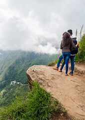 Fototapeta premium A couple of young people on the edge of a mountain cliff admiring a valley in the clouds on the island of Sri Lanka