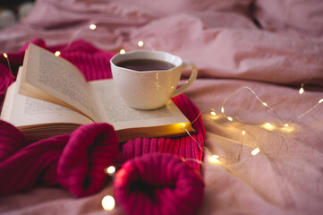 Tasty cup of tea with knitte cloth and open book in bed. Good morning. Selective focus.