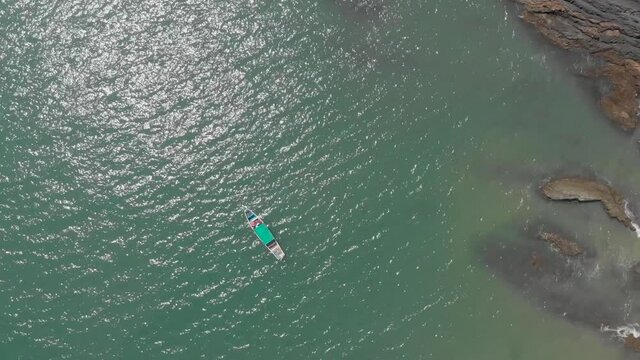 This is a drone of two fishing boats in the Indian Ocean next to a rocky beach. This was filmed near Gokarna, India. The blue clear ocean water is visible.