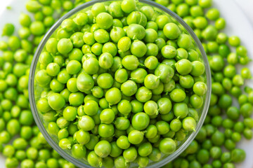 Close up fresh green peas in a glass bowl and pods on a white background