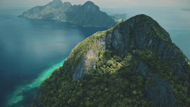 Mountain top with green forest at azure ocean water. Small hilly islets at sea bay. Majestic nobody landscape at Palawan Island, El Nido, Philippines, Asia. Cinematic drone shot at summer day