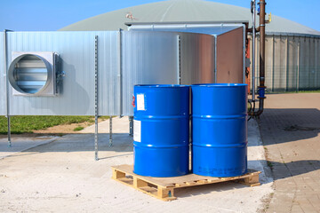 2 big blue barrels stand on a wooden pallet in front of a biogas plant