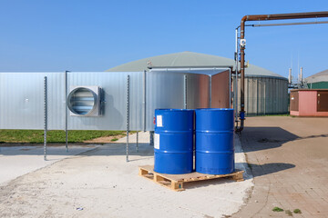 2 big blue barrels stand on a wooden pallet in front of a biogas plant