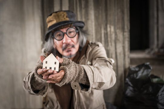 Focus to hands and wood house. Homeless senior man wearing sweater, hat, gloves and glasses with hold small wooden house because dream and want have about shelter for myself. Help and hope concept.