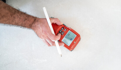Bauarbeiter spürt mit dem Detektor die unsichtbaren Rohre der Fußbodenheizung auf