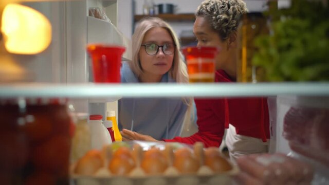 Two diverse girls looking in fridge taking pudding for snack