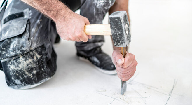 Bauarbeiter schl&auml;gt mit Hammer und Meissel ein Loch in den Estrich um die Feuchtigkeit des Estrichs zu messen