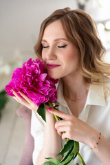 woman in shirt and jeans, holds bouquet of peonies in her hands, looking at flowers. Portrait of beautiful blonde woman. Surprise bouquet of flowers for date, mothers day or valentines day.