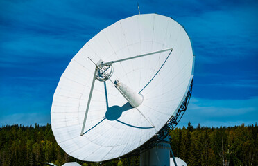 Large white radio radar disc with blue skies and trees in the background.