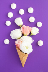 Ice cream cone with pink and white flowers and white meringue on the violet background