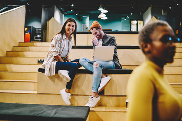 Prosperous male and female hipsters discussing ideas and laughing during freelance job on laptop,...