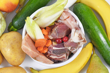 Top view of bowl with dog food consisting of raw beef and chicken meat, salmon fish, fruits and vegetables surrounded by healthy ingredients 