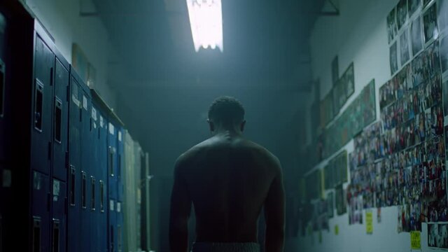 A male athlete standing in a locker room hits a wall with his hand
