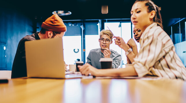 Multiracial skilled colleagues watching tutorial webinar for courses e learning during cooperation meeting in modern workspace, male and female freelancers analyzing web information from laptop
