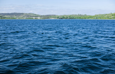 Wunderschöne Sommerlandschaft auf dem See, tiefblaues Wasser, mit kleinen Wellen und kleinem Wald auf dem Land.