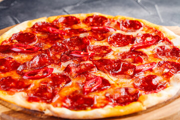 Pepperoni pizza on wooden board on dark background. Close-up