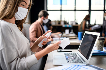 People with face masks disinfecting indoors in office, back to work after coronavirus lockdown.